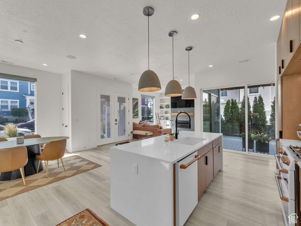 Kitchen featuring white appliances, light wood-style flooring, a kitchen island with sink, a textured ceiling, and light countertops