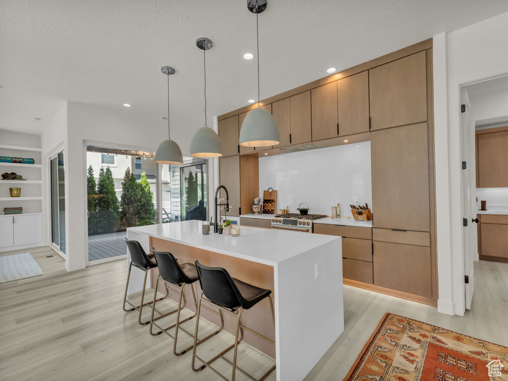 Kitchen with light wood-style floors, light countertops, a center island with sink, a kitchen bar, and pendant lighting