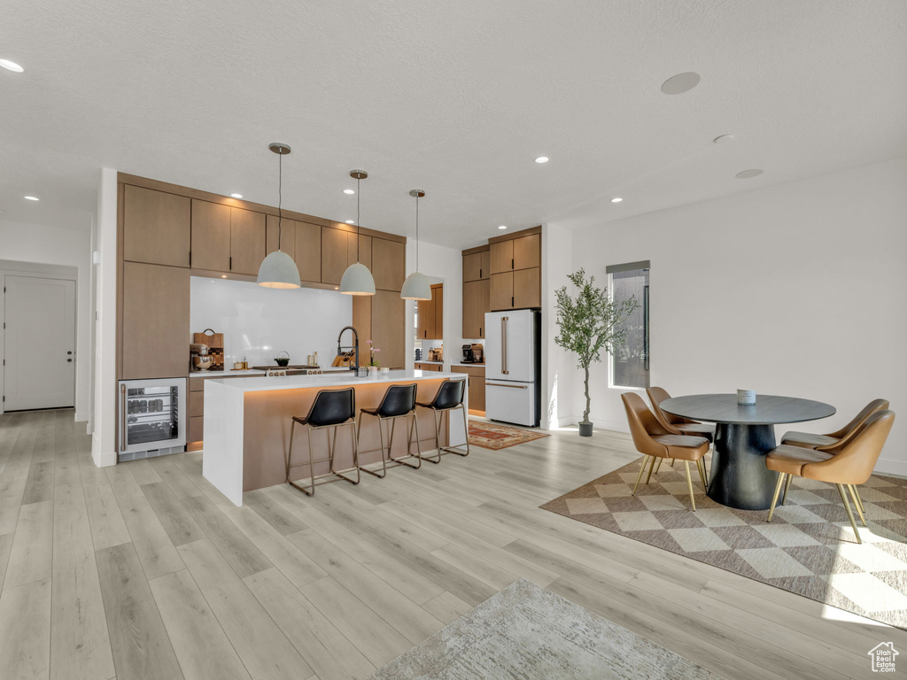 Kitchen with freestanding refrigerator, wine cooler, light wood-type flooring, a kitchen bar, and recessed lighting
