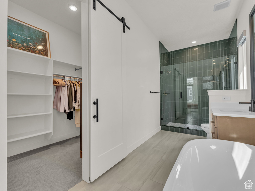 Bathroom with a stall shower, a walk in closet, vanity, a freestanding bath, and recessed lighting