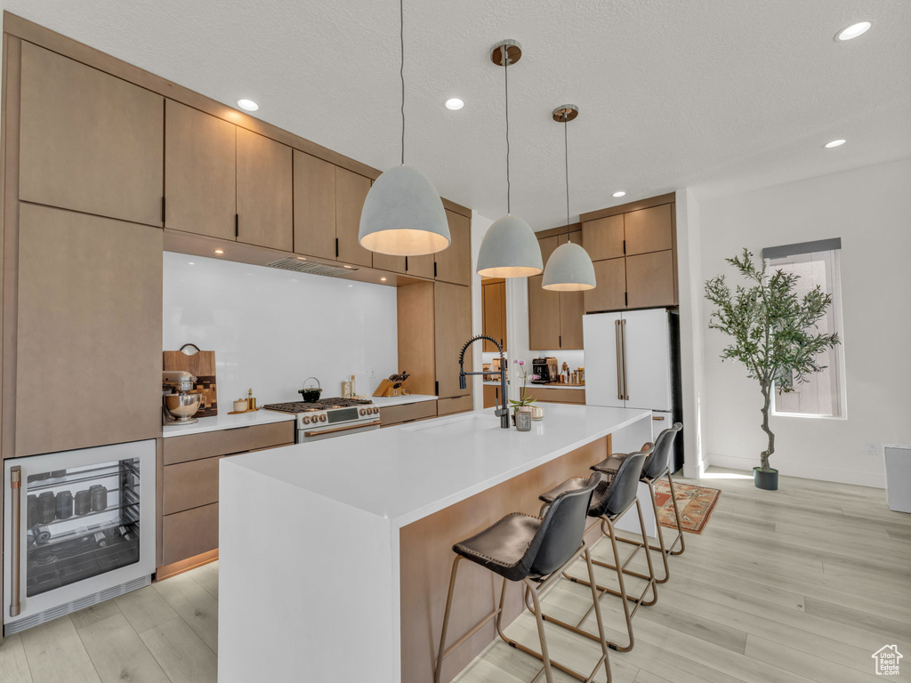 Kitchen featuring high end stainless steel range, freestanding refrigerator, light wood-type flooring, wine cooler, and light countertops