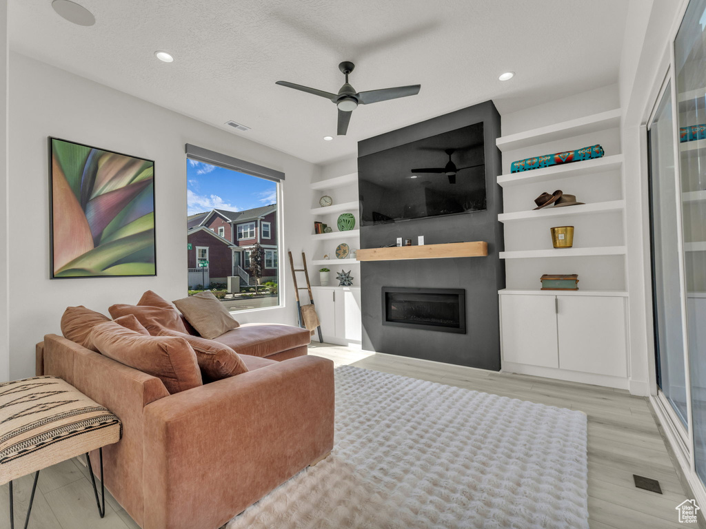 Living area featuring a glass covered fireplace, a ceiling fan, light wood-style floors, recessed lighting, and built in shelves