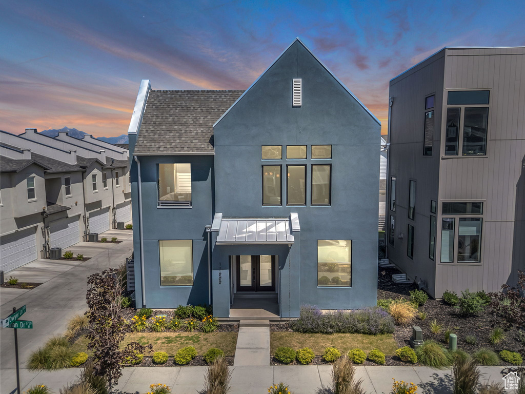 View of front of house with stucco siding, a shingled roof, driveway, and a garage