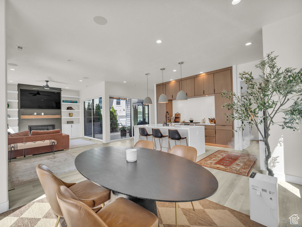 Dining area featuring light wood-style flooring, ceiling fan, recessed lighting, a glass covered fireplace, and built in shelves