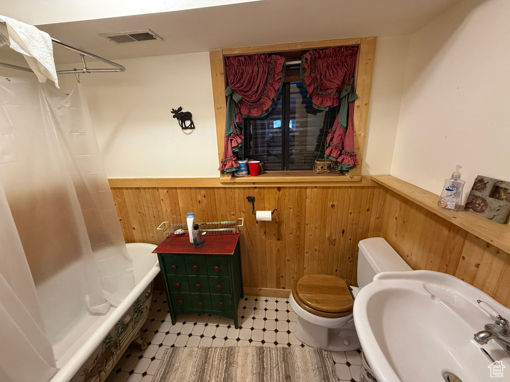 Bathroom featuring a wainscoted wall, wood walls, tile patterned floors, and shower / bathtub combination with curtain