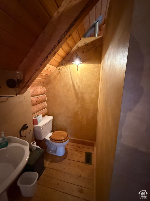 Bathroom with rustic walls, hardwood / wood-style flooring, and a wood ceiling with exposed beams