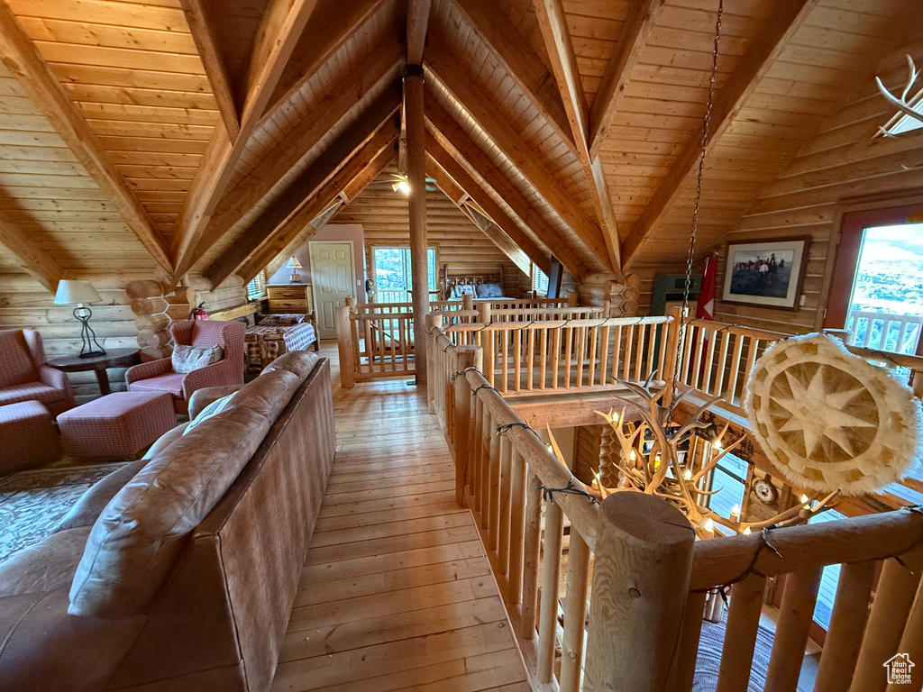 Living area with an upstairs landing, light wood-type flooring, wooden ceiling, rustic walls, and a chandelier