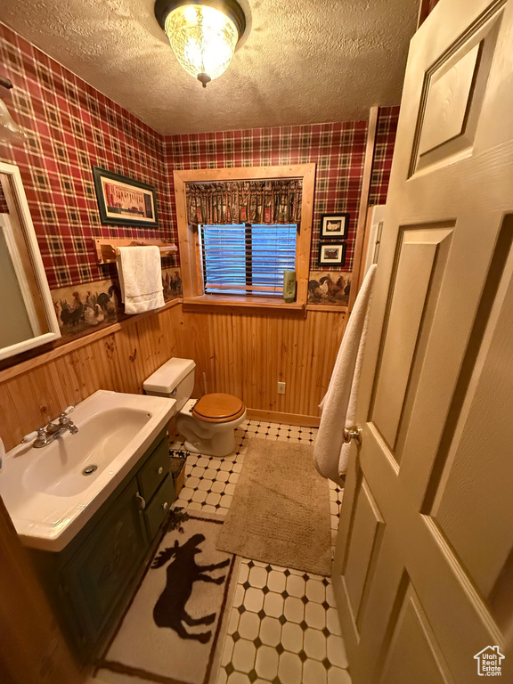 Half bathroom featuring tile patterned floors, wainscoting, wallpapered walls, a textured ceiling, and vanity