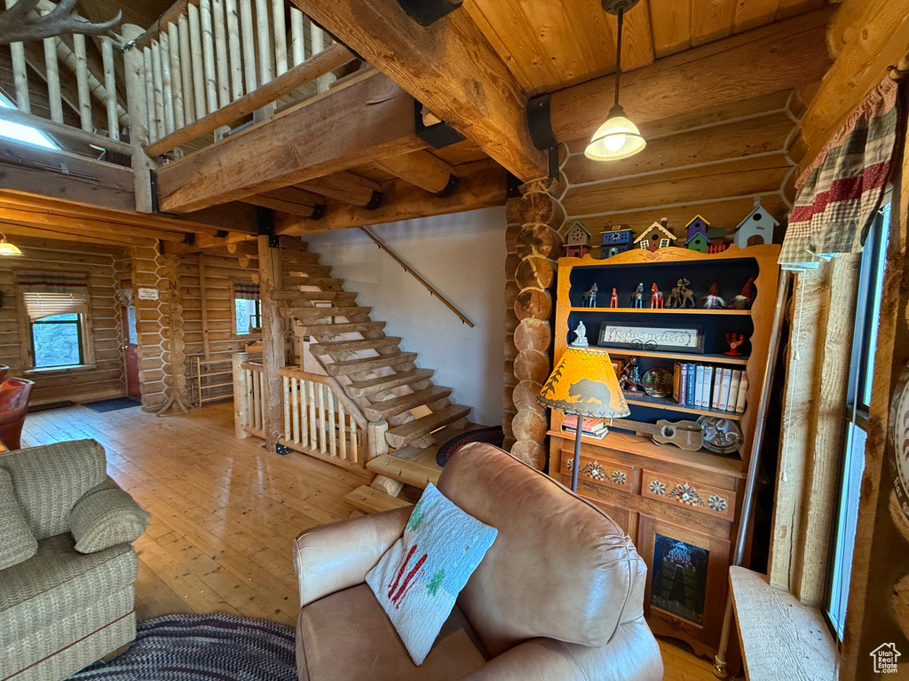 Living area with log walls, hardwood / wood-style floors, a wood ceiling with exposed beams, and stairway