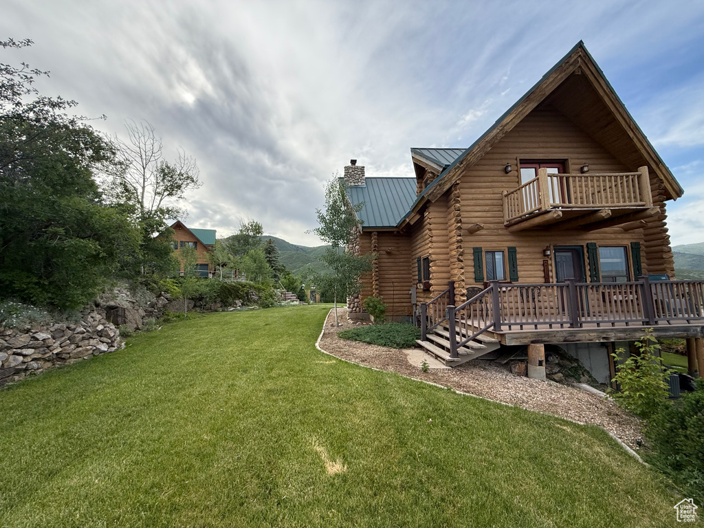 View of grassy yard featuring a balcony and a deck with mountain view