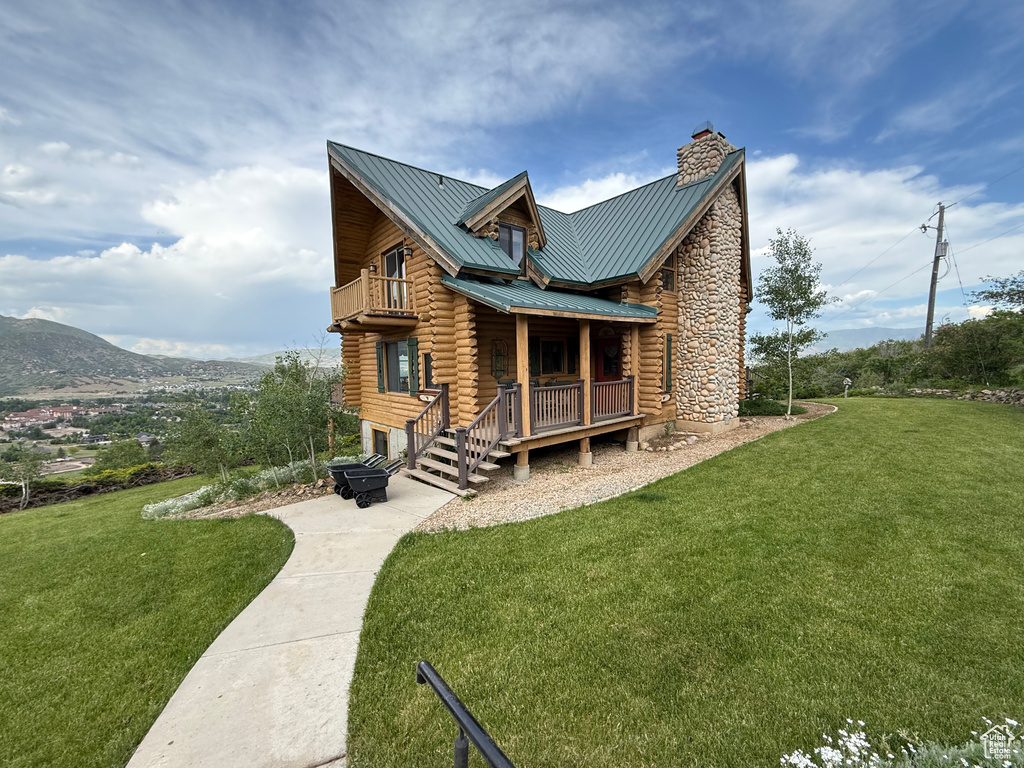 Rear view of property featuring log exterior, a balcony, a chimney, and a yard