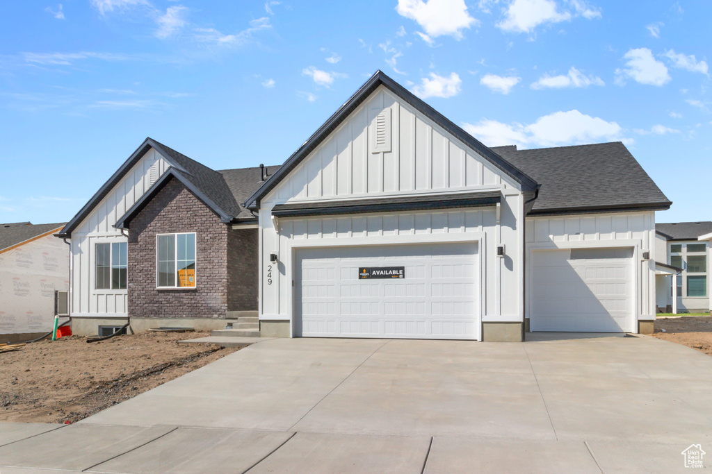 View of front of home with board and batten siding, an attached garage, driveway, and a shingled roof