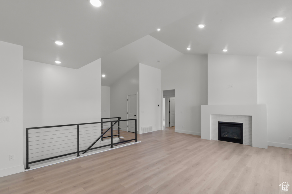 Unfurnished living room featuring wood finished floors, high vaulted ceiling, recessed lighting, and a tiled fireplace