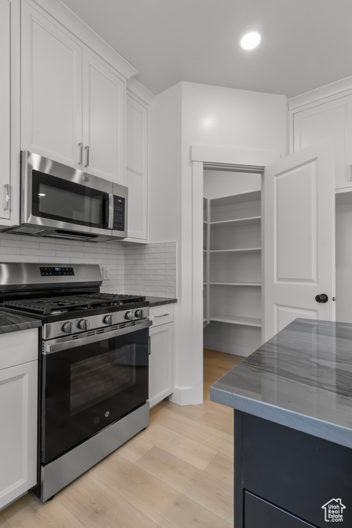 Kitchen featuring appliances with stainless steel finishes, dark countertops, white cabinetry, and tasteful backsplash