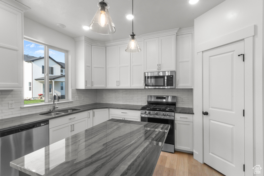 Kitchen featuring appliances with stainless steel finishes, white cabinetry, tasteful backsplash, hanging light fixtures, and dark stone countertops