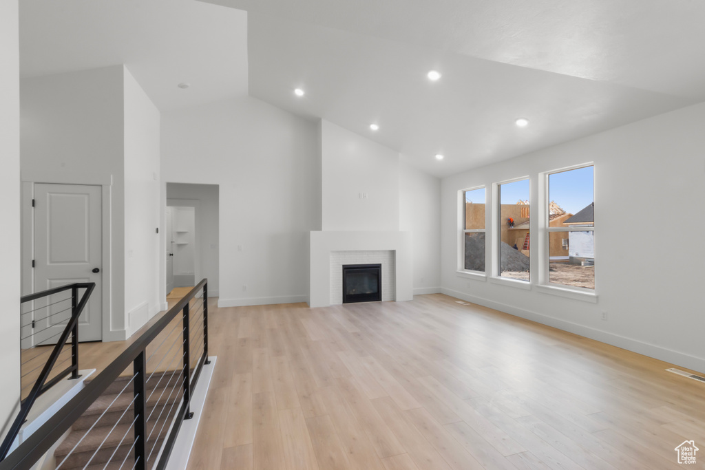 Unfurnished living room featuring a glass covered fireplace, light wood-style floors, high vaulted ceiling, and recessed lighting