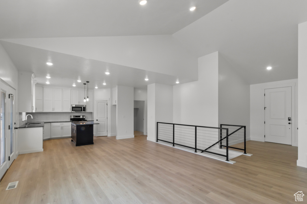 Kitchen featuring stainless steel appliances, dark countertops, white cabinets, a center island, and recessed lighting