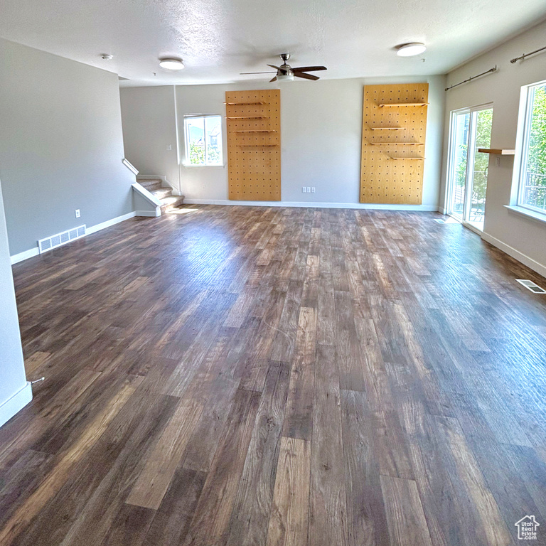 Unfurnished living room featuring dark wood-style flooring, stairs, and ceiling fan