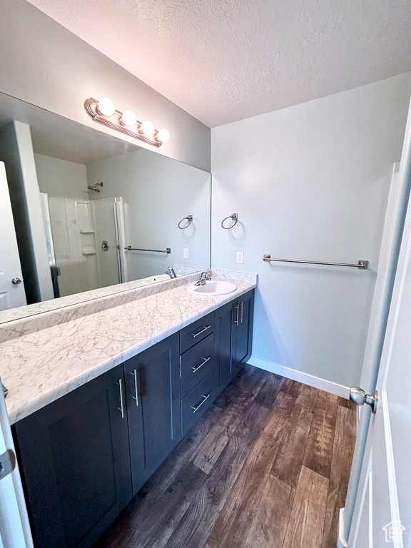 Bathroom featuring wood finished floors, double vanity, a shower with shower door, and a textured ceiling
