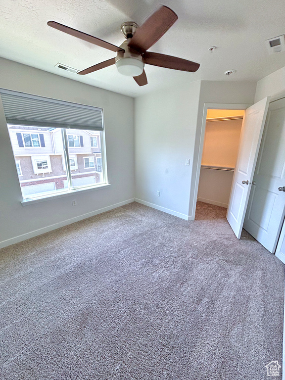 Unfurnished bedroom with carpet floors, ceiling fan, a textured ceiling, and a walk in closet