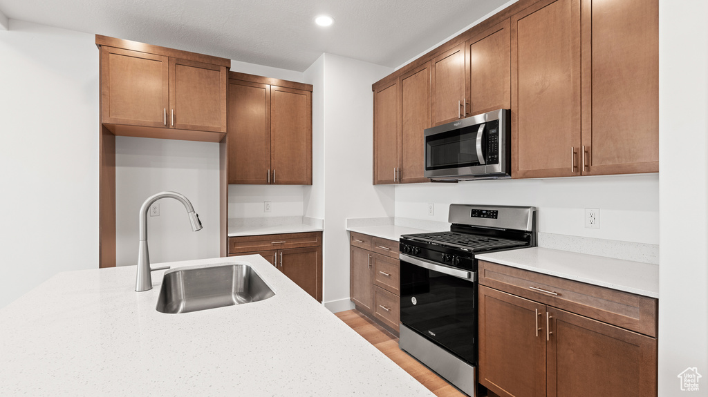 Kitchen with stainless steel appliances, light wood-style flooring, recessed lighting, and brown cabinetry