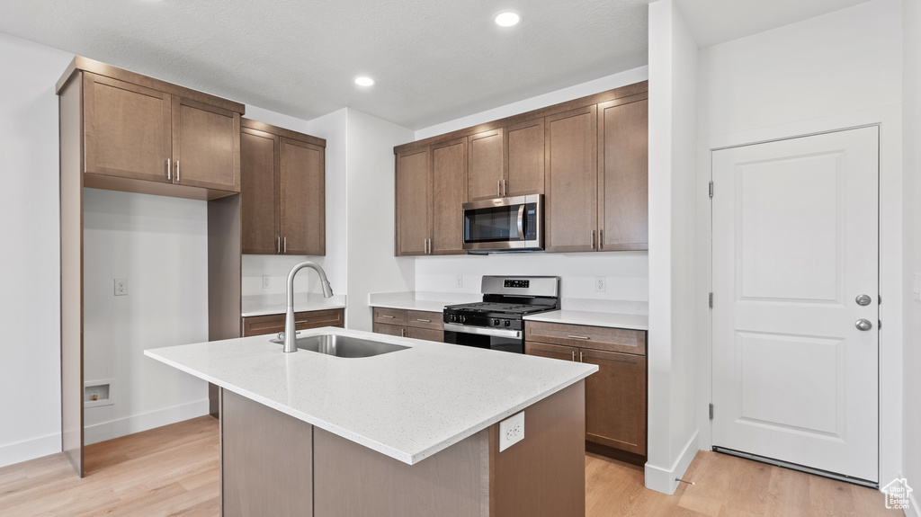 Kitchen with appliances with stainless steel finishes, light wood-style flooring, an island with sink, and recessed lighting