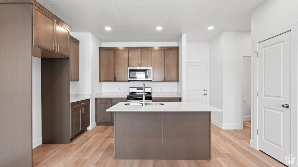 Kitchen featuring appliances with stainless steel finishes, light wood-style flooring, a center island with sink, light countertops, and recessed lighting