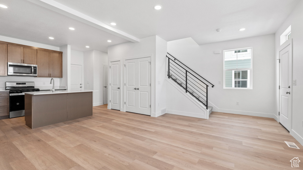 Kitchen with stainless steel appliances, light wood-style floors, recessed lighting, light countertops, and a kitchen island with sink