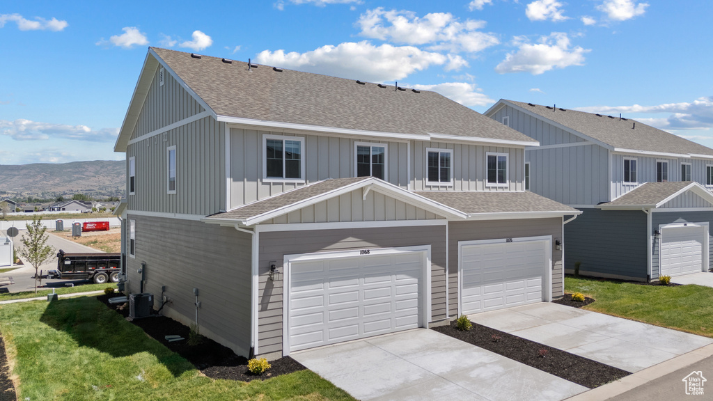 View of property with board and batten siding, a shingled roof, concrete driveway, an attached garage, and a front lawn