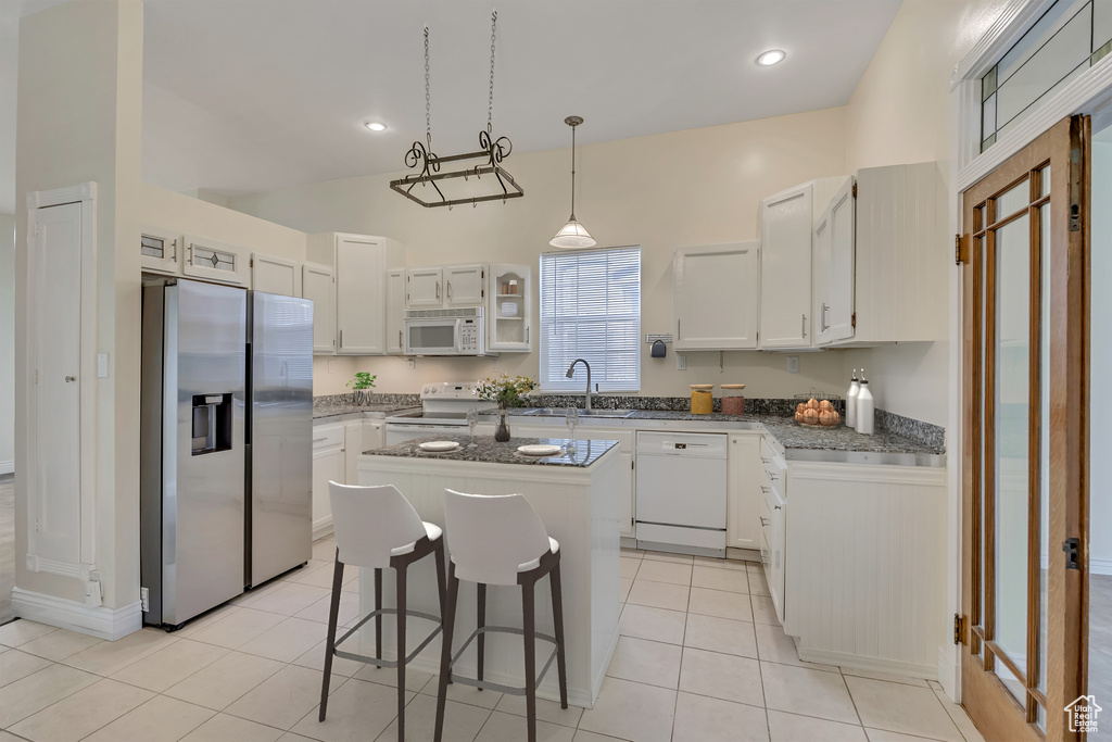 Kitchen featuring white appliances, a center island, a kitchen breakfast bar, and light tile patterned floors