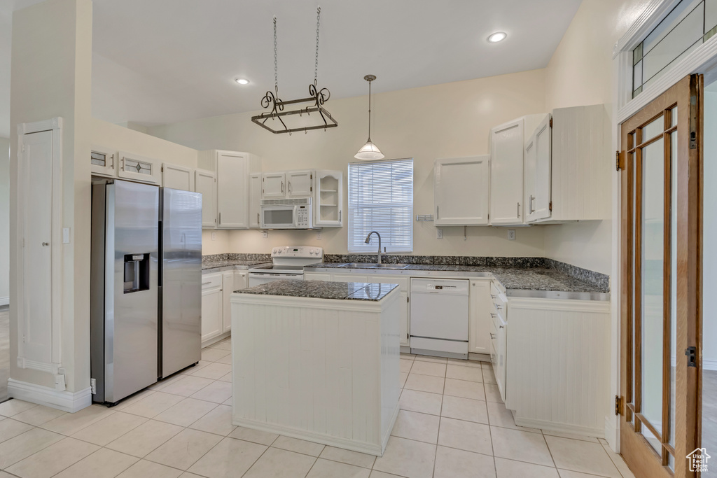 Kitchen featuring white appliances, a center island, white cabinets, hanging light fixtures, and light tile patterned floors