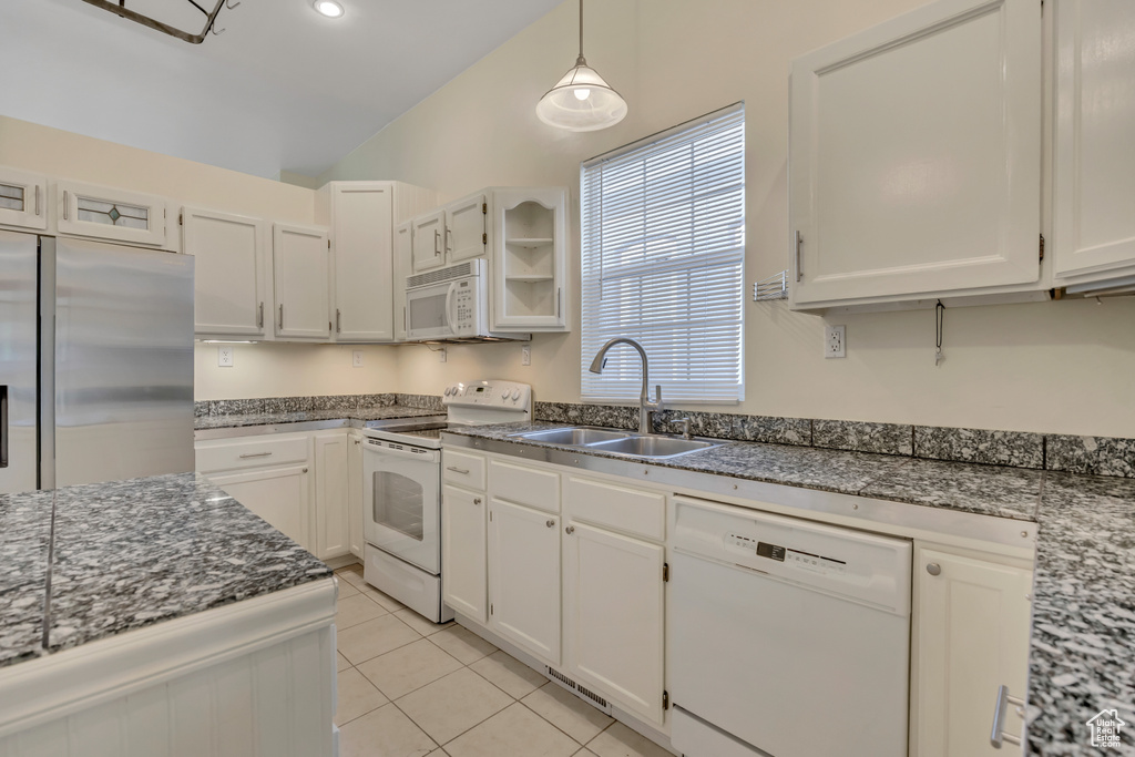 Kitchen featuring white appliances, lofted ceiling, light tile patterned flooring, dark stone countertops, and decorative light fixtures