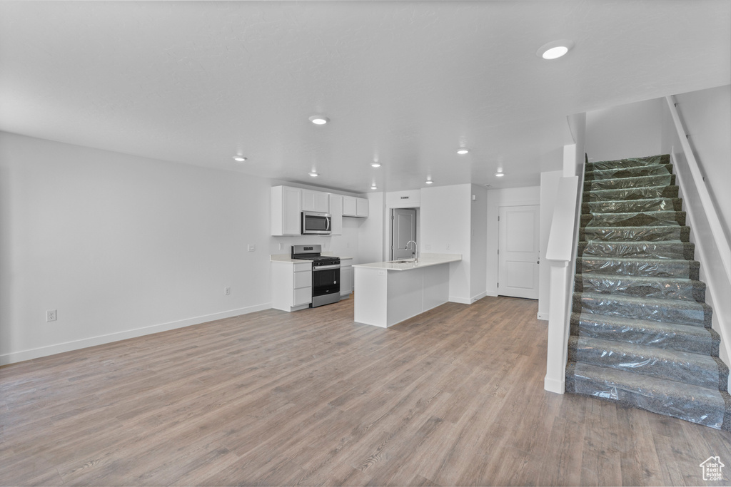 Unfurnished living room with stairs, light wood-style flooring, and recessed lighting