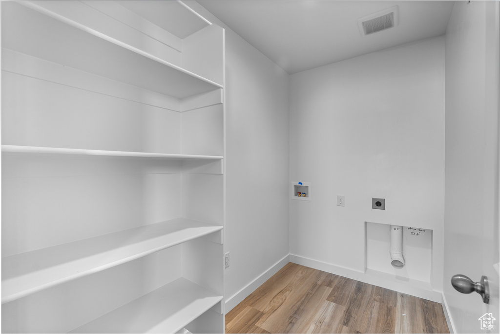 Washroom with electric dryer hookup, hookup for a washing machine, and wood finished floors