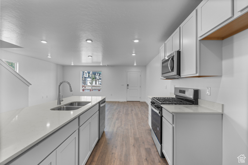 Kitchen with stainless steel appliances, recessed lighting, wood finished floors, light stone countertops, and white cabinets