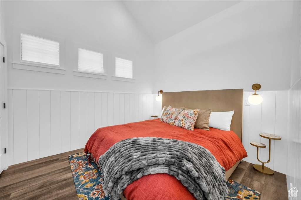 Bedroom featuring wood finished floors, vaulted ceiling, and wainscoting