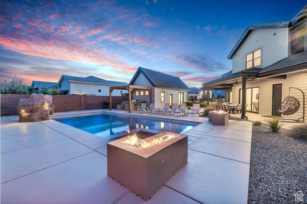 Pool at dusk featuring an outdoor fire pit, a patio, an outbuilding, an exterior structure, and a fenced backyard