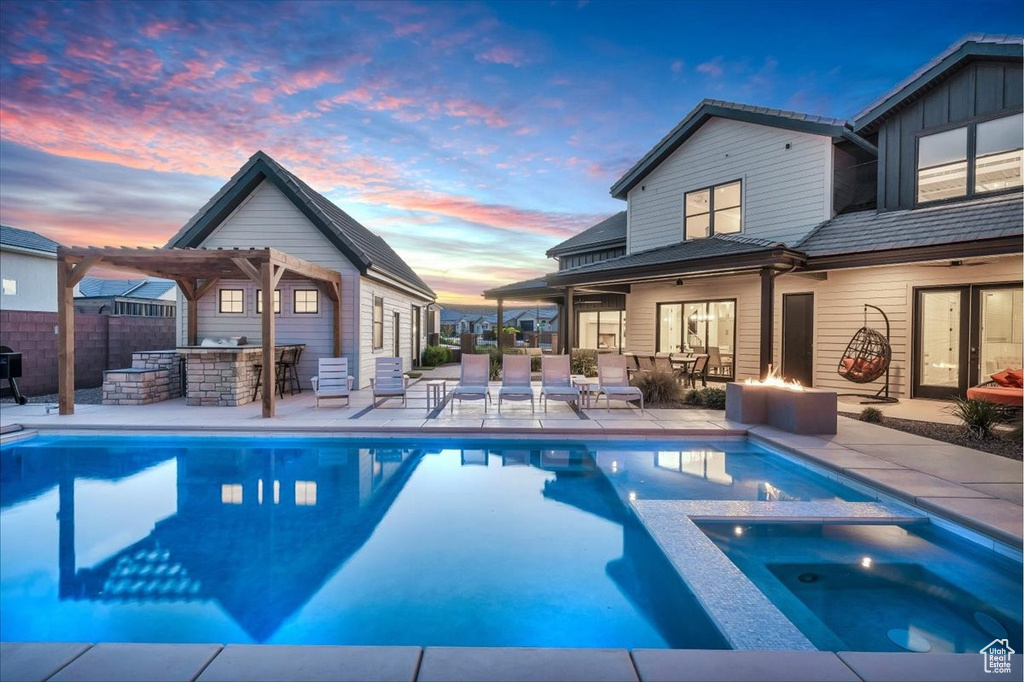 Pool at dusk with a pool with connected hot tub, a patio, exterior kitchen, and a pergola