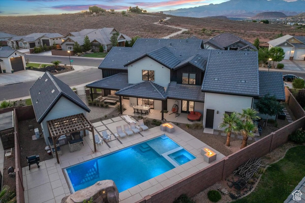 Back of property at dusk featuring a fenced backyard, a pool with connected hot tub, an outdoor living space, a mountain view, and a residential view