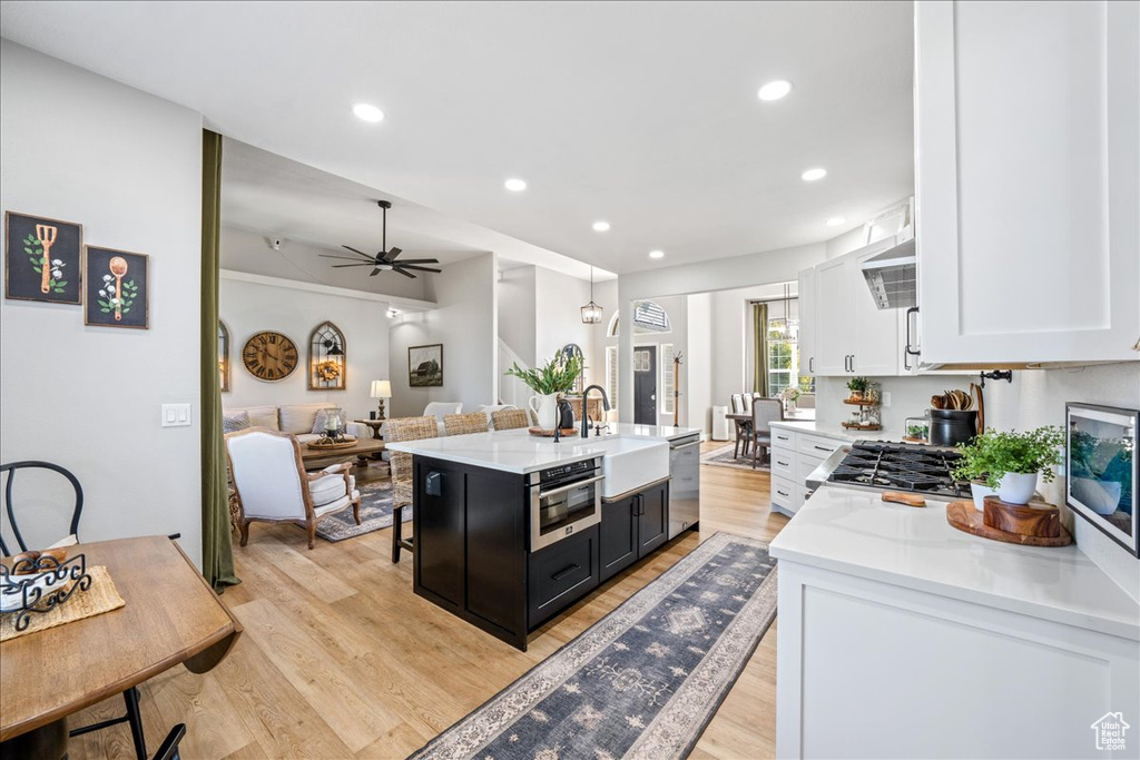 Kitchen featuring stainless steel dishwasher, white cabinetry, a center island with sink, light wood-style floors, and open floor plan