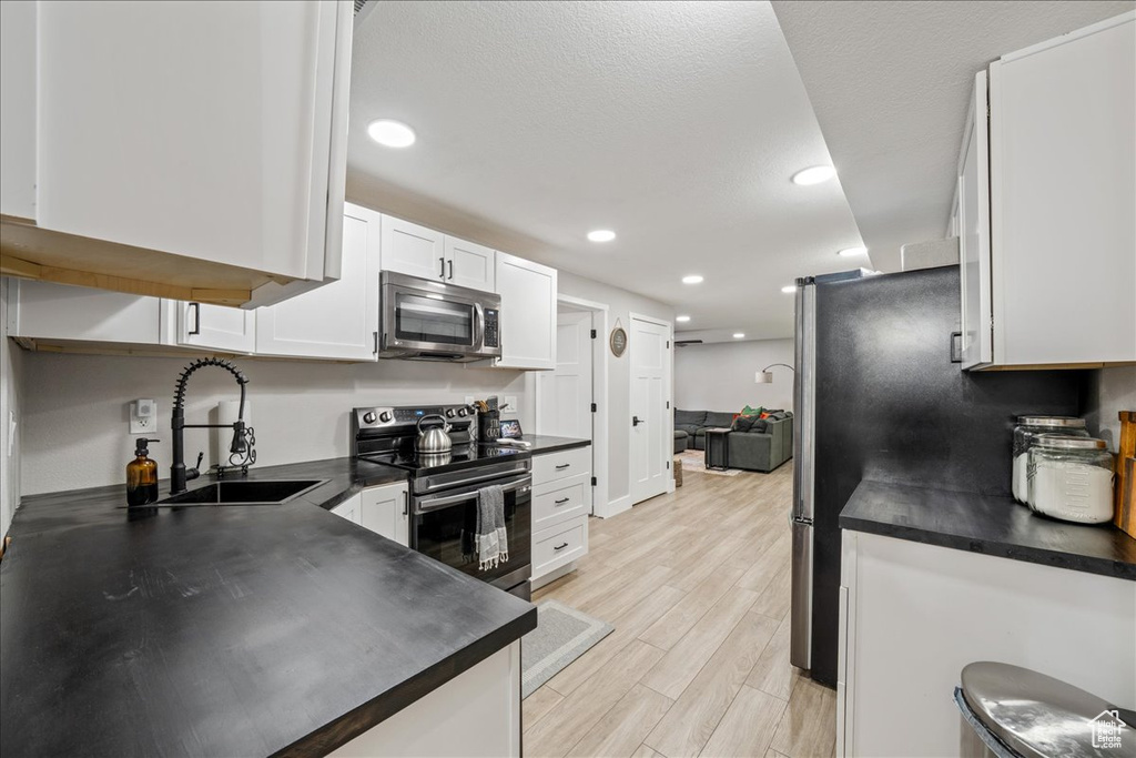 Kitchen with stainless steel appliances, dark countertops, white cabinetry, light wood-style flooring, and recessed lighting