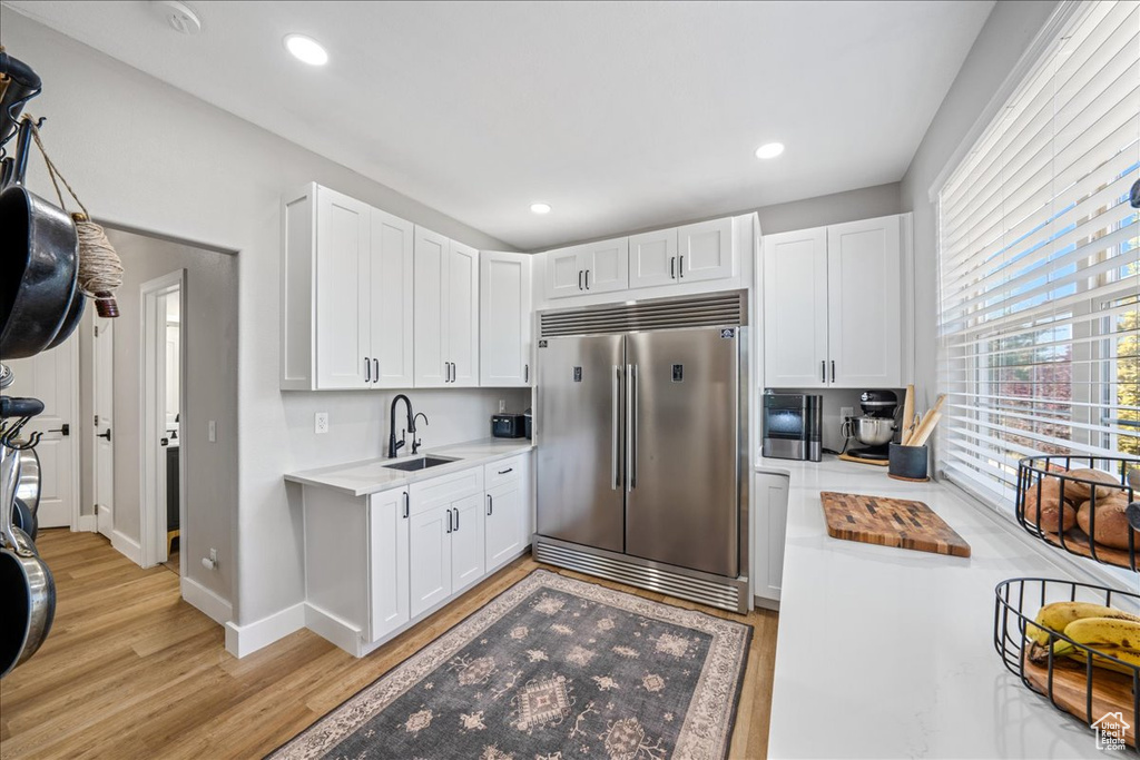 Kitchen featuring built in refrigerator, light wood-type flooring, light countertops, white cabinets, and recessed lighting