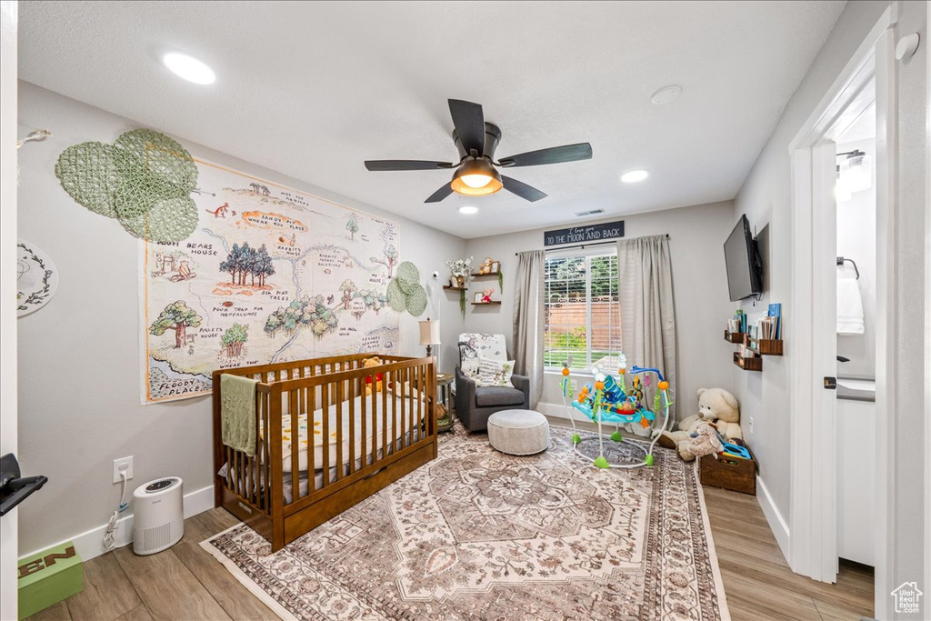 Bedroom with a crib, light wood-style floors, ceiling fan, and recessed lighting