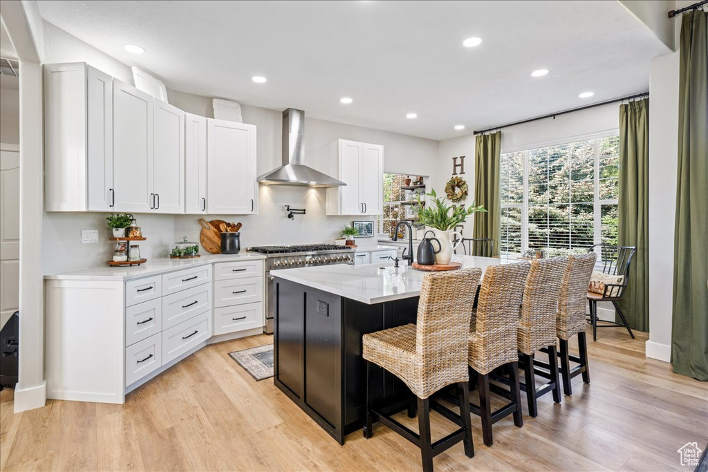 Kitchen with wall chimney range hood, stainless steel range, light wood finished floors, a kitchen bar, and recessed lighting