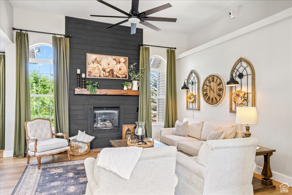 Living room with ceiling fan, a large fireplace, and wood finished floors