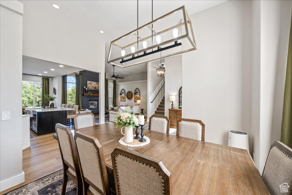 Dining space with stairway, a glass covered fireplace, ceiling fan, light wood-type flooring, and recessed lighting
