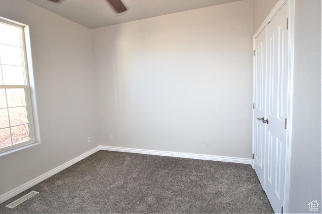 Unfurnished room with dark colored carpet and a ceiling fan