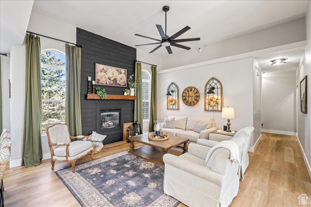 Living area with a ceiling fan, light wood finished floors, and a large fireplace