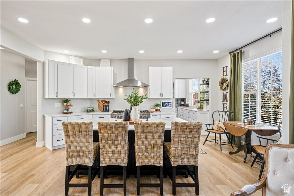 Kitchen featuring wall chimney exhaust hood, light countertops, light wood-style floors, a breakfast bar area, and recessed lighting