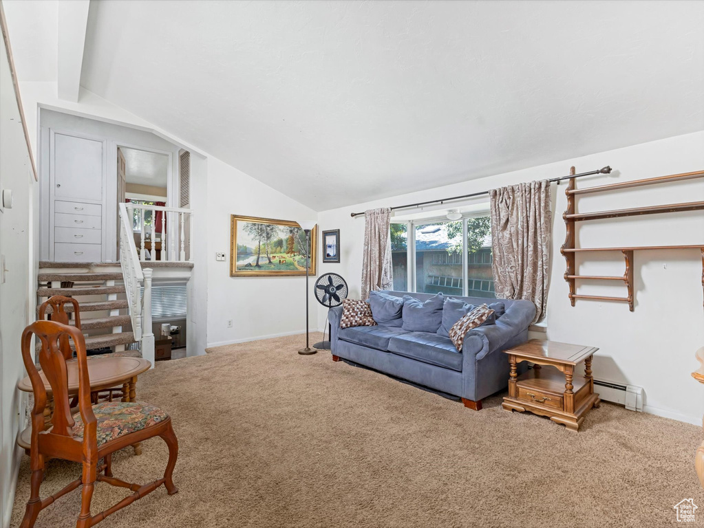 Carpeted living area featuring vaulted ceiling, a baseboard heating unit, and stairs